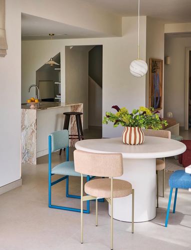Dining nook with round white pedestal table, blue and pink chairs, striped vase, kitchen beyond