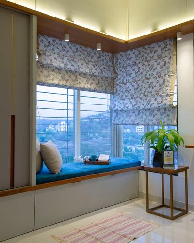 Teal upholstered corner window seat with floral roman blinds overlooking a hillside city view