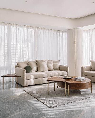 Beige sofa with round walnut coffee tables in a sunlit living room with sheer curtains