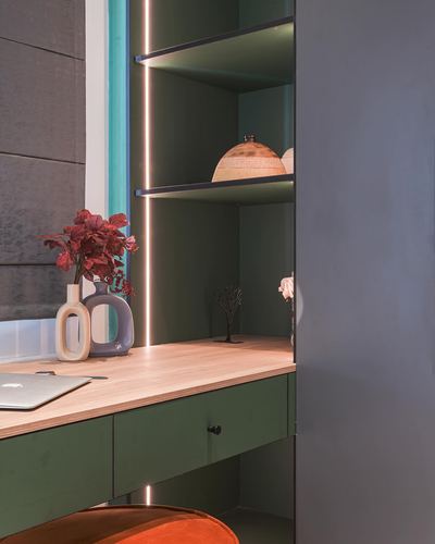 Green study nook with backlit shelves, wooden desk, laptop and ceramic vases