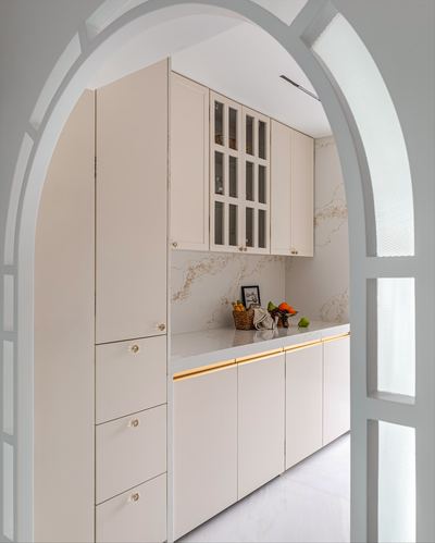 View through arched doorway into a soft beige kitchen with veined stone backsplash and brass trim