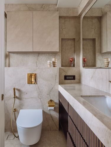 Marble bathroom with fluted wood vanity, brass fittings, and wall-hung toilet