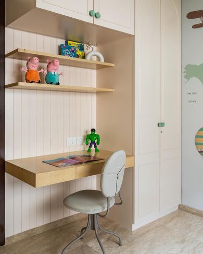 Child's study nook with floating wooden desk, shelves with toys, and mint-knobbed wardrobe