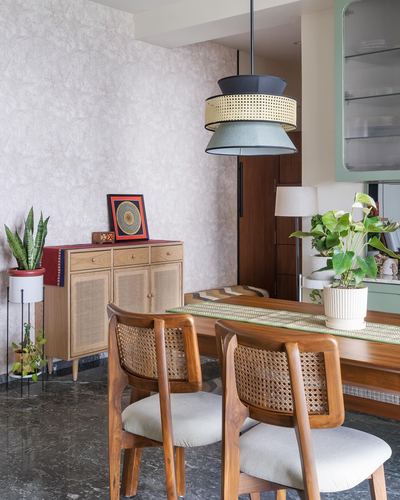 Dining nook with cane-back teak chairs, layered pendant light, and rattan-front sideboard against textured wallpaper