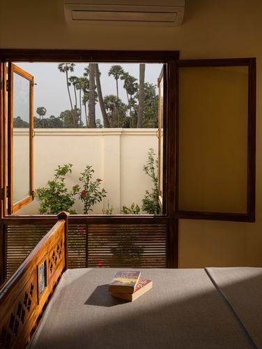 Wooden bed with carved headboard beside open window overlooking garden and palm trees