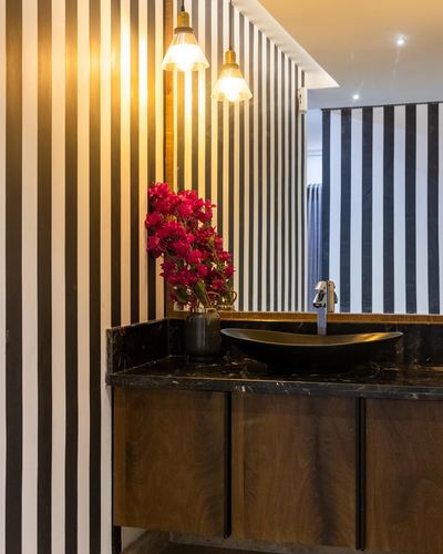 Bathroom vanity with black stone counter, boat sink, wood cabinetry, striped black and white wall, pendant lights.