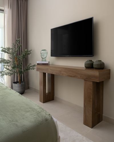 Bedroom with chunky wood console under wall-mounted tv, olive throw and potted plant beside curtain