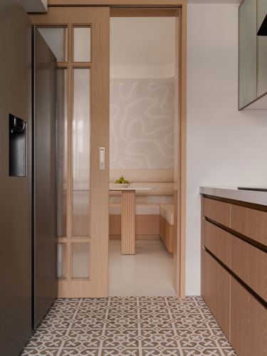 Kitchen with patterned floor tile beside sliding wood door opening to an oak dining nook with sculpted wall.
