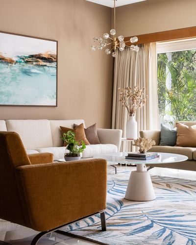 Living room with cream sofa, rust armchair, round marble table, chandelier and blue palm-print rug