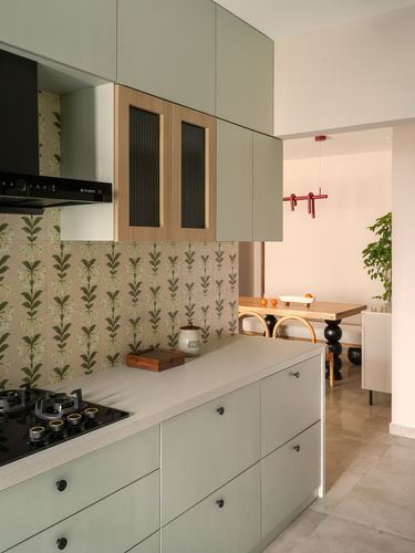 Sage green kitchen with patterned backsplash opening to a dining nook beyond