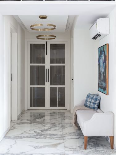 Marble-floored foyer with glazed double doors, brass ring pendants, and an upholstered bench beneath framed art