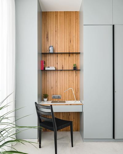Built-in wooden desk nook with open shelves set into a sage-green cabinetry wall
