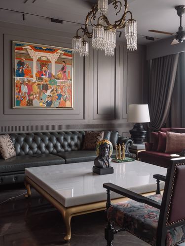 Grey paneled living room with tufted leather sofa, marble coffee table, and crystal chandelier