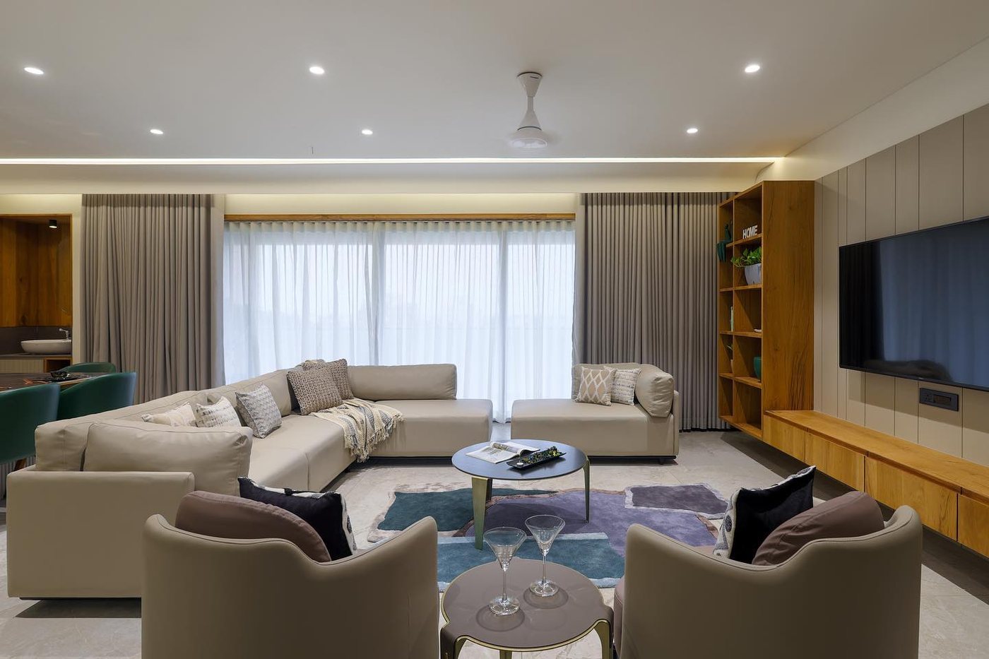 Beige sectional living room with round marble coffee table, wooden shelving and wall-mounted tv