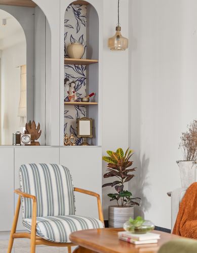 Living room corner with arched wallpapered niche, striped armchair, and amber pendant light