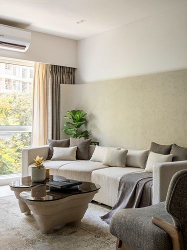 Beige sectional sofa against textured plaster wall with sculptural stone coffee tables and window view of trees