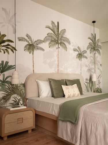 Bed with upholstered headboard against palm tree mural wall, cane nightstand beside it