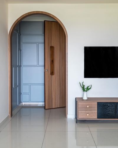 Arched wooden door opens to a blue-grey paneled passage beside a tv console in a living room
