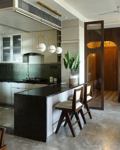 Mumbai kitchen with dark marble island, ribbed cabinetry, brass globe pendants and cane bar chairs