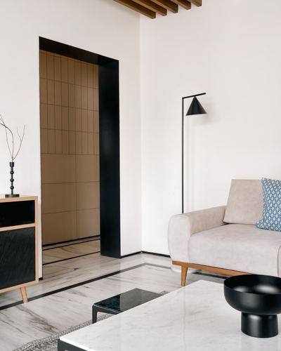 Minimalist living room corner with beige sofa, black arc lamp, marble floor and tiled doorway