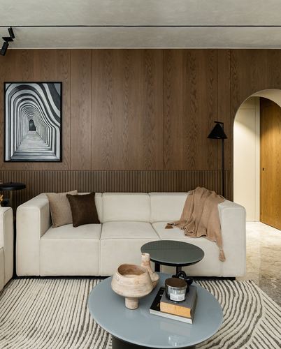 Beige sectional sofa against ribbed wood-panelled wall with arched doorway and round coffee tables