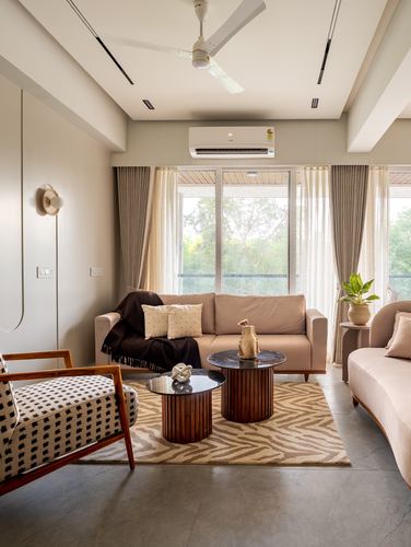 Neutral living room with pink sofas, drum coffee tables, and a zebra rug under a large window