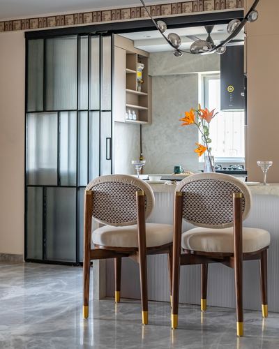 Two cane-back wooden dining chairs with brass-tipped legs before a marble kitchen counter with orange lilies.