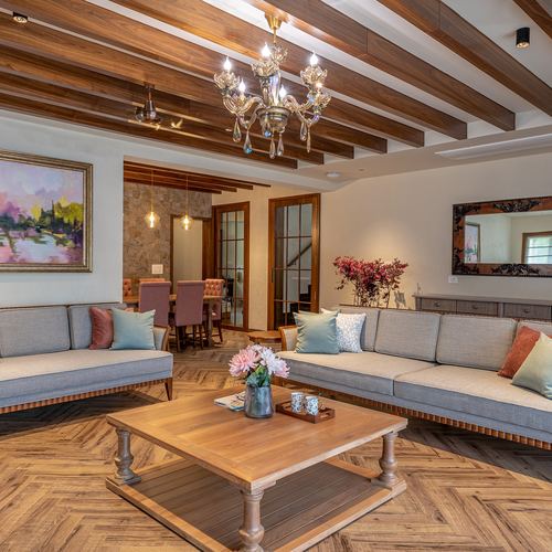 Living room with wood beam ceiling, crystal chandelier, herringbone floor and gray sectional sofas