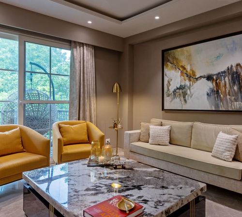 Living room with mustard armchairs, beige sofa, marble coffee table and abstract painting on beige wall
