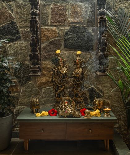 Brass Krishna and Radha idols on wooden altar against stone wall with incense smoke and flowers
