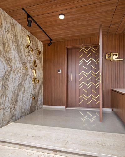 Entrance foyer with wood-paneled ceiling, marble wall with brass sculptures, and chevron brass-inlaid wooden door