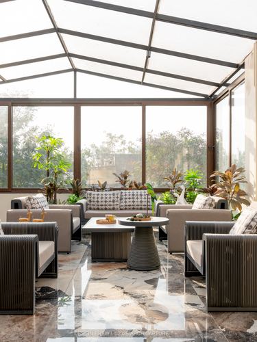 Glass-roofed terrace lounge with grey ribbed sofas around a round table and plants