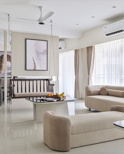 Beige living room with curved sofas, marble coffee table, and a hanging wooden swing bench
