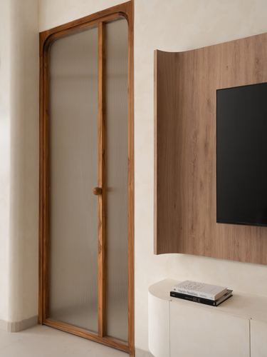 Arched fluted glass door beside curved wooden tv panel in a softly lit living room