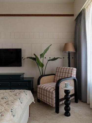 Bedroom corner with checked cane armchair, black bobbin table and lamp beside a plant and paneled wall