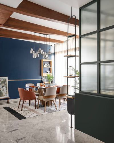 Dining area with navy wall, exposed wood beams, silver pendant cluster, and marble floor