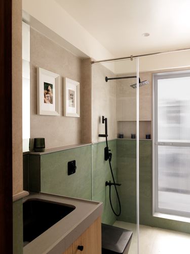 Bathroom with sage green stone tiling, black fixtures, glass shower partition and framed prints on wall
