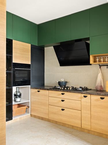 Modern kitchen corner with green upper cabinets, wood lower cabinets, black hood, and ribbed backsplash