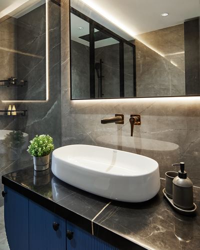 Grey marble bathroom vanity with oval white basin, brass fixtures, and backlit mirror over blue fluted cabinetry