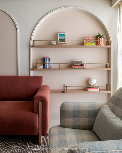 Arched wall niche with brass-edged wood shelves beside terracotta and check armchairs