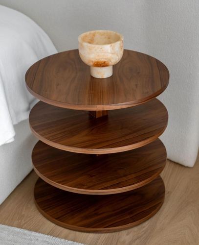Round tiered wooden side table with a stone bowl beside a white bed