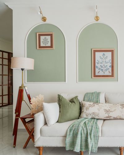 Cream sofa with green cushions beneath two arched sage-green wall niches with framed art