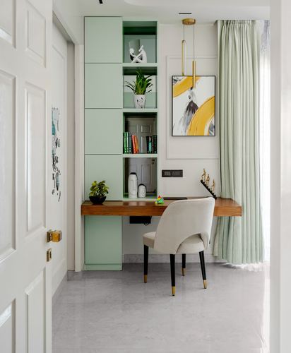 Small study nook with sage-green cabinets, wood desk, cream chair and abstract art