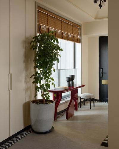 Cream hallway with a red curved console table, potted plant, and bamboo blind window