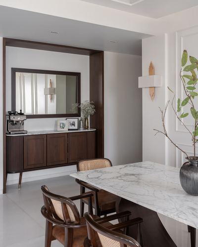 Dining area with marble table, cane chairs, and a mirrored dark-wood console nook beyond