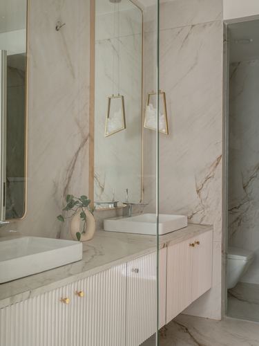Marble bathroom with twin vessel sinks, arched mirrors, brass pendants, and fluted cabinetry