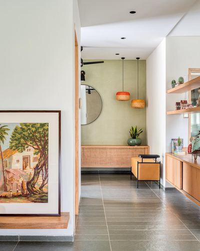Foyer passage with leaning framed painting, sage nook, round mirror and rattan pendant lights