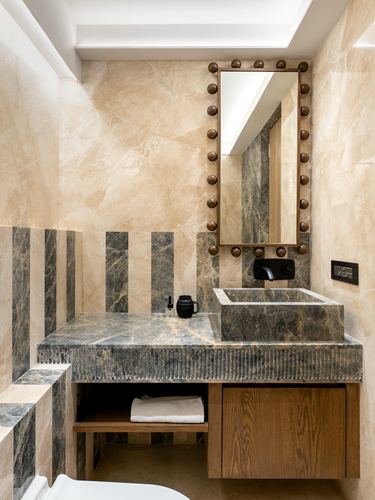 Bathroom vanity with dark grey vessel sink, striped marble backsplash, and studded bronze mirror.