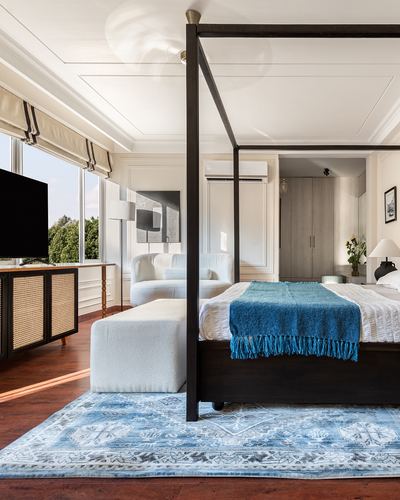 Bedroom with black four-poster bed, blue throw, boucle bench, and blue medallion rug on wood floor