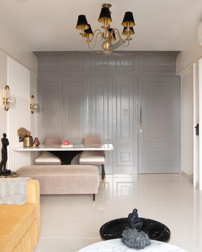 Living-dining space with brass chandelier, grey paneled wall, marble table and mustard sofa